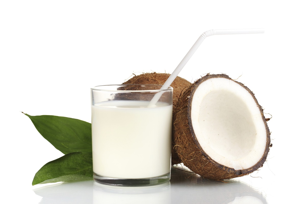 Glass of coconut milk next to open coconut