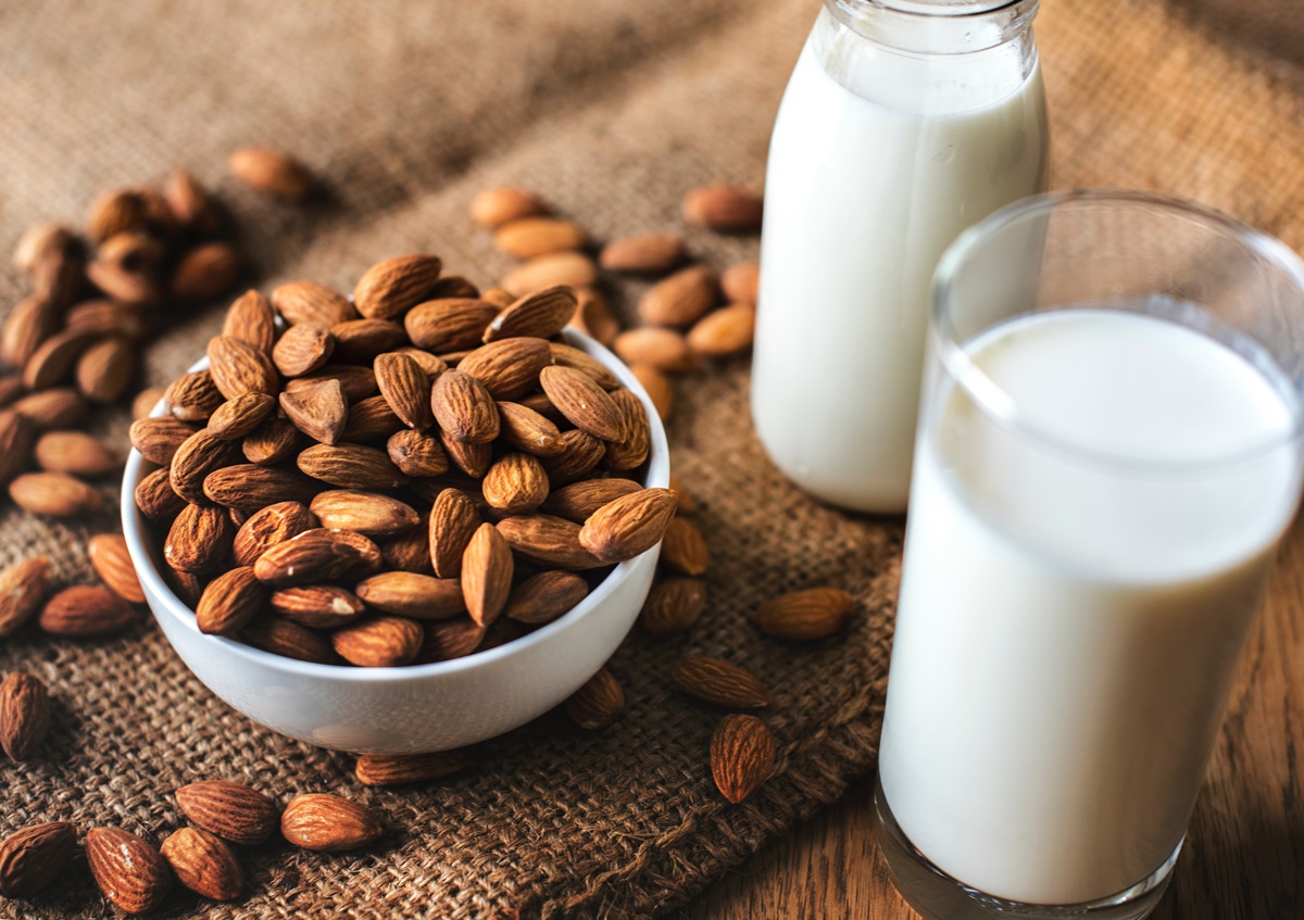 Almonds in a bowl next to glass of almond milk